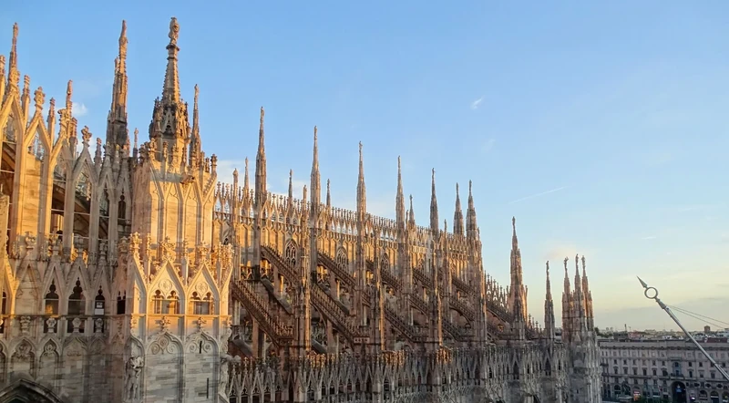Rows of rooftop statues and spires on the Duomo against a blue Milan sky